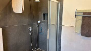 Eine moderne Dusche mit Glastür, einer Handbrause und einem wandmontierten Handtuchhalter.