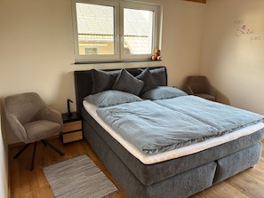 A bedroom with a bed, a chair, a nightstand, a window, and a wall with a sign. - Holiday Home 'Ferienhaus Thomes' in Hunsrück (Külz (Hunsrück))