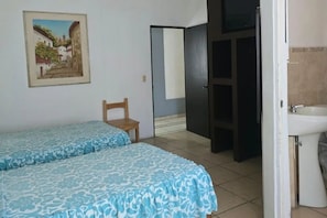Une chambre avec deux lits, une chaise, un tableau et une salle de bain avec un lavabo.
