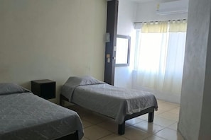 Une chambre avec deux lits, une petite table de chevet, une fenêtre avec des rideaux et un appareil de climatisation.