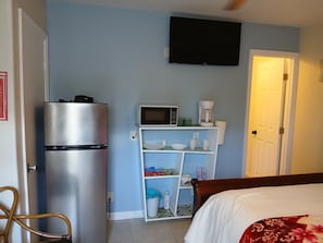 Quarto com cama, televisão na parede, geladeira, micro-ondas e máquina de café em uma prateleira.