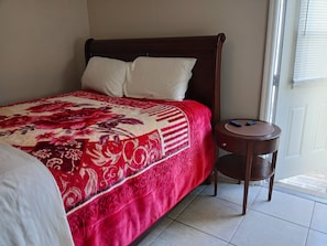 Uma cama com colcha floral em vermelho e branco, cabeceira de madeira e mesa de cabeceira com controle remoto.