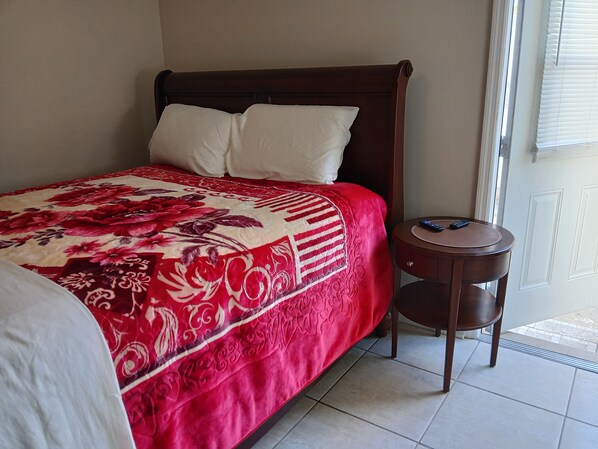A bed with a red and white floral bedspread, a wooden headboard, and a bedside table with a remote control. - New Listing (Tampa)