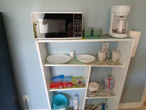 A kitchen area with a microwave, coffee maker, and shelves containing plates, bowls, and kitchen utensils. - New Listing (Tampa)