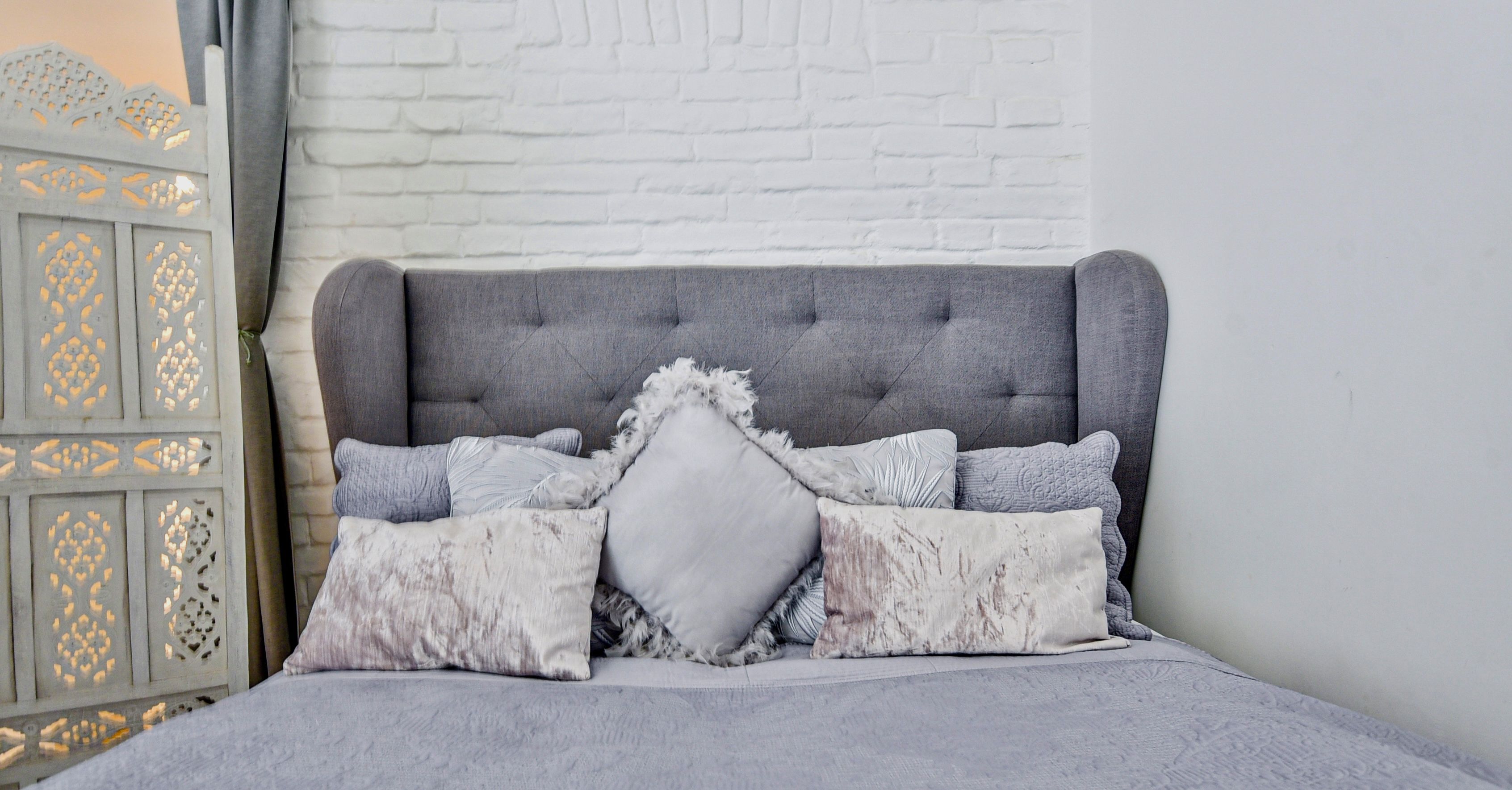 A bed with a tufted headboard, multiple pillows, and a decorative wall panel.