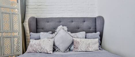 A bed with a tufted headboard, multiple pillows, and a decorative wall panel.