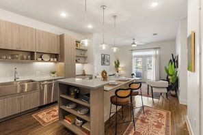A modern kitchen with a central island, pendant lighting, and a view to the living area. - Sophisticated 1BR w/ Stylish Escape SHI-2207 (Austin)