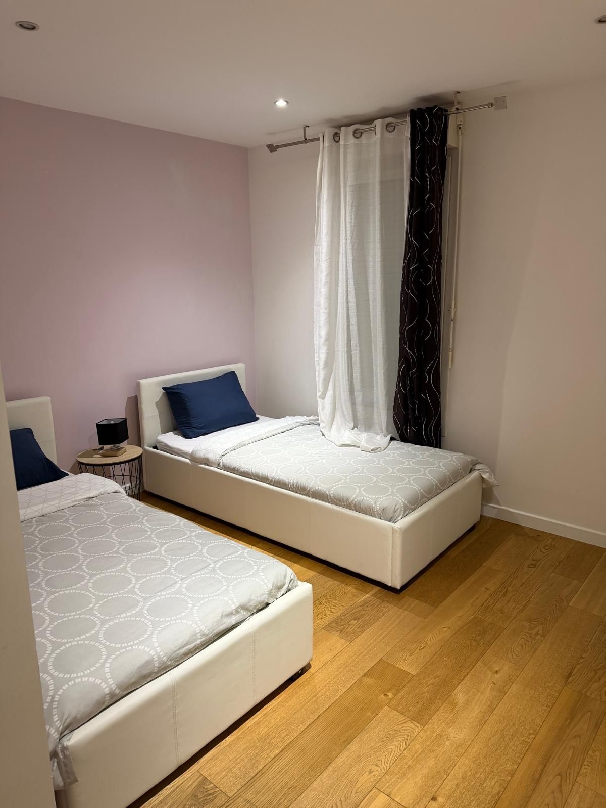 A bedroom with two beds, a nightstand, and a curtain.