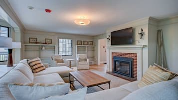 A spacious living room with a fireplace, comfortable seating, and a flat-screen TV mounted above it.