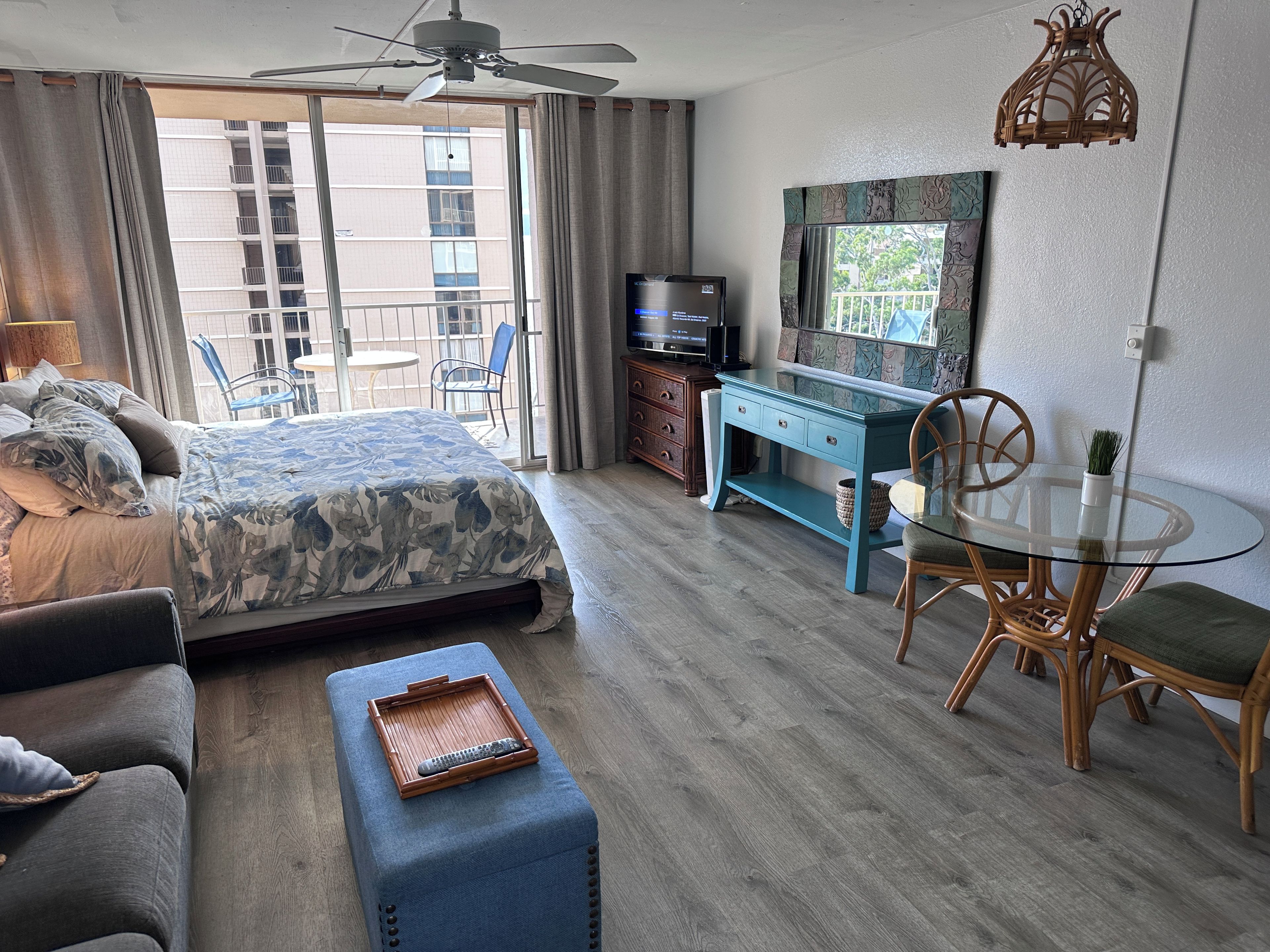 A hotel room with a bed, a desk, a chair, a table, and a ceiling fan.