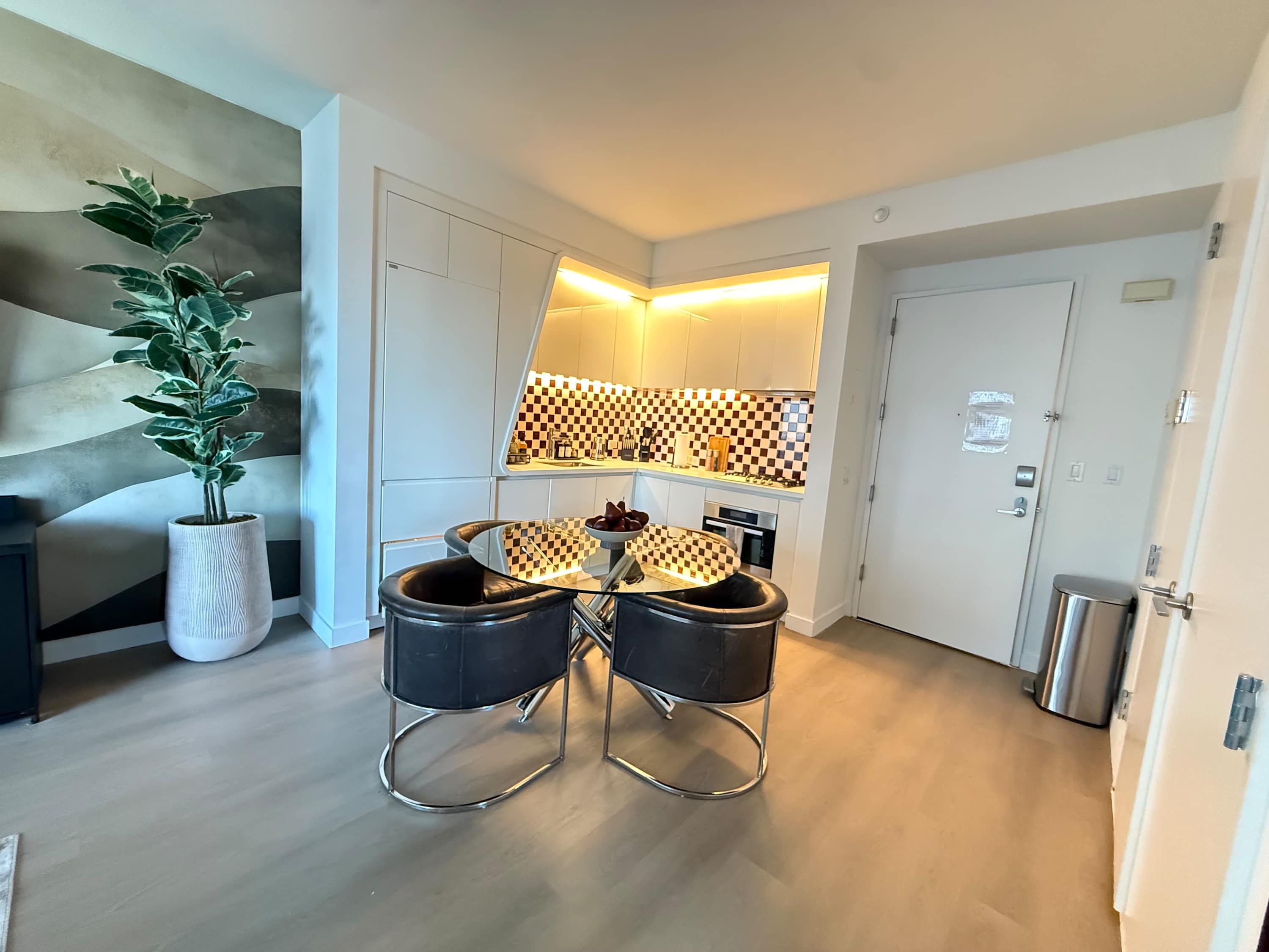 A modern kitchen with a checkered backsplash, a dining table with black chairs, and a potted plant.