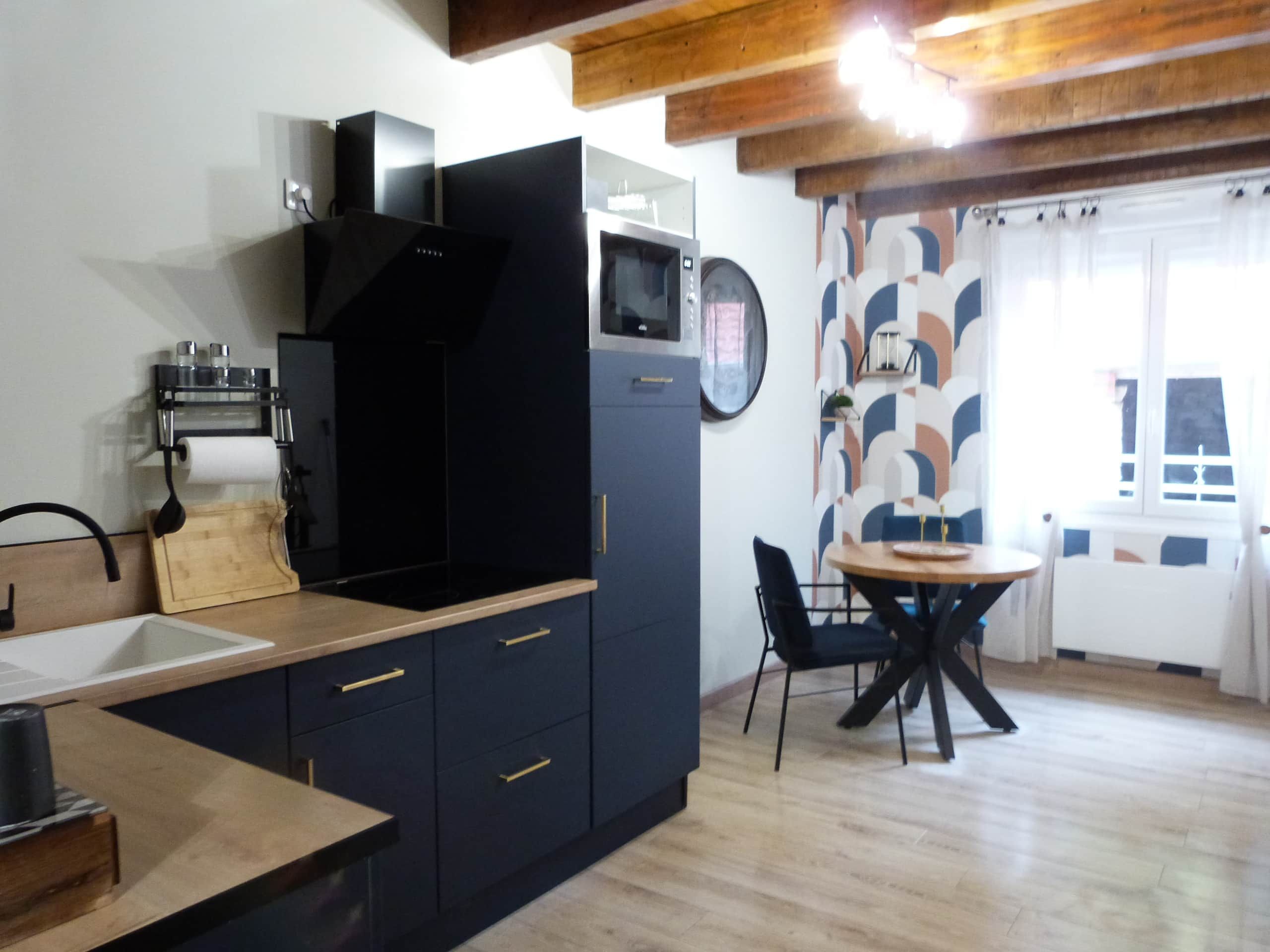 Cocina compacta con armarios oscuros, un microondas y una tabla de cortar de madera.