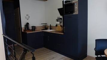 Een compacte keuken met donkere kastjes, een magnetron, een koffiezetapparaat en een klein aanrecht.
