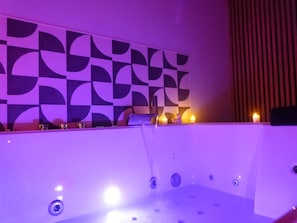 Una bañera con pared de diseño geométrico, un grifo y velas.