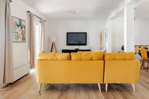 Uma sala de estar com sofá seccional, televisão de tela plana, abajur e mesa de pebolim.