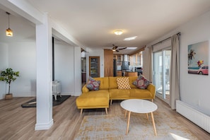 Una sala de estar moderna con un sofá amarillo, una mesa de centro blanca y vista a la cocina.