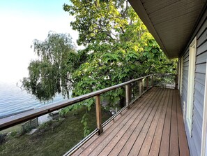 Um deck de madeira com guarda-corpo de vidro, com vista para a água e árvores.