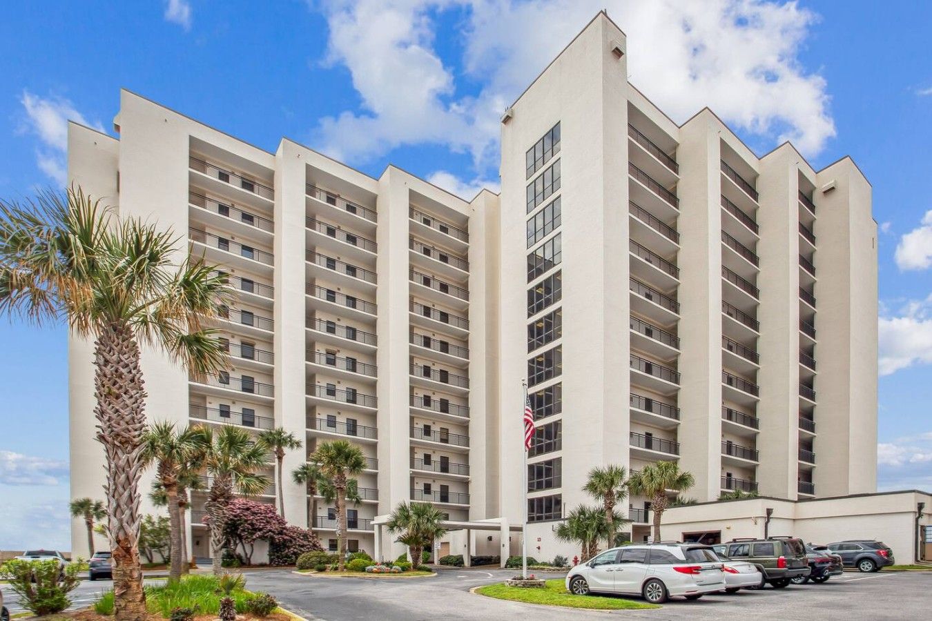 A multi-story hotel with a central courtyard, parking area, and a flagpole.