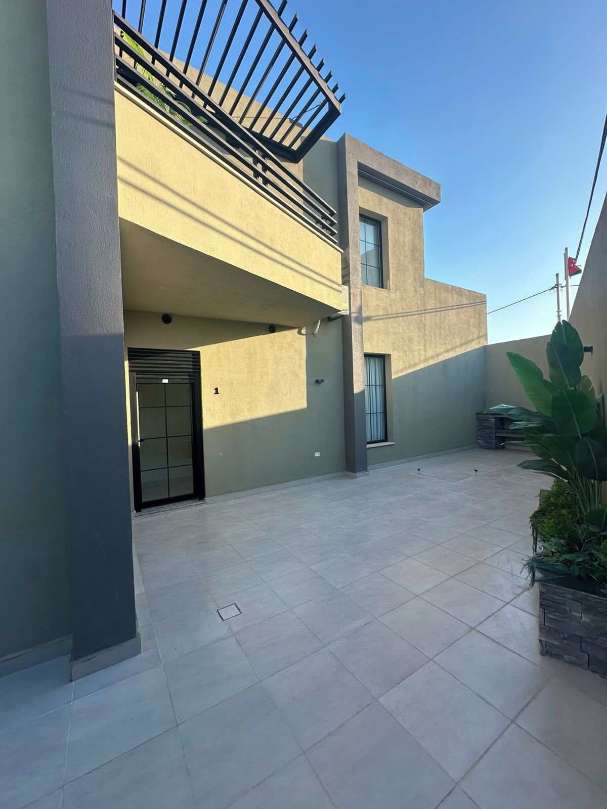 A modern building with a flat roof, a balcony, and a tiled courtyard.
