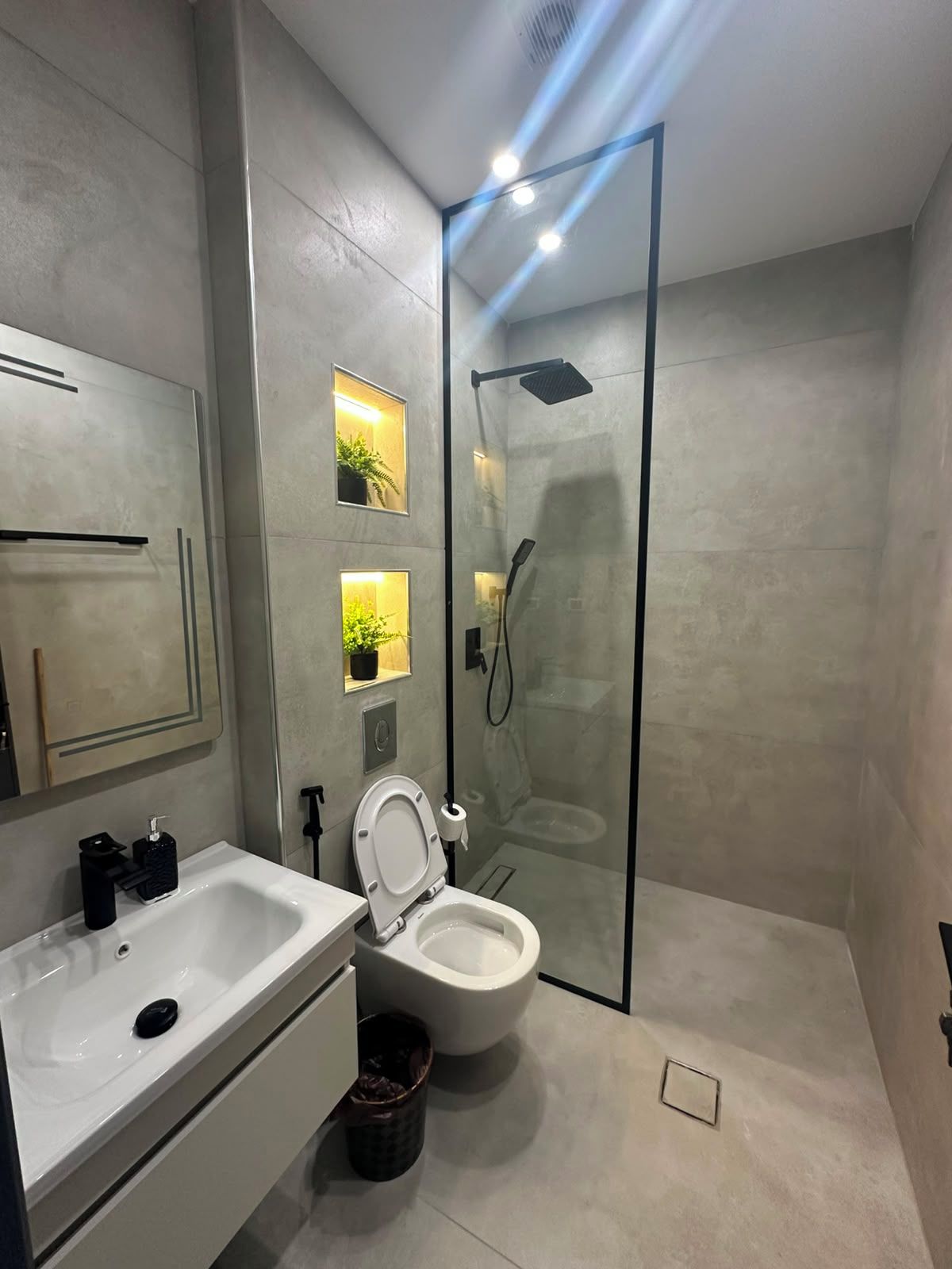 A modern bathroom with a glass-enclosed shower, a white sink, and a toilet.