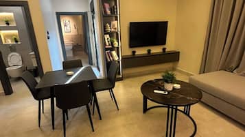 Un salon moderne comprenant un canapé, un téléviseur, une table à manger avec des chaises et une bibliothèque.
