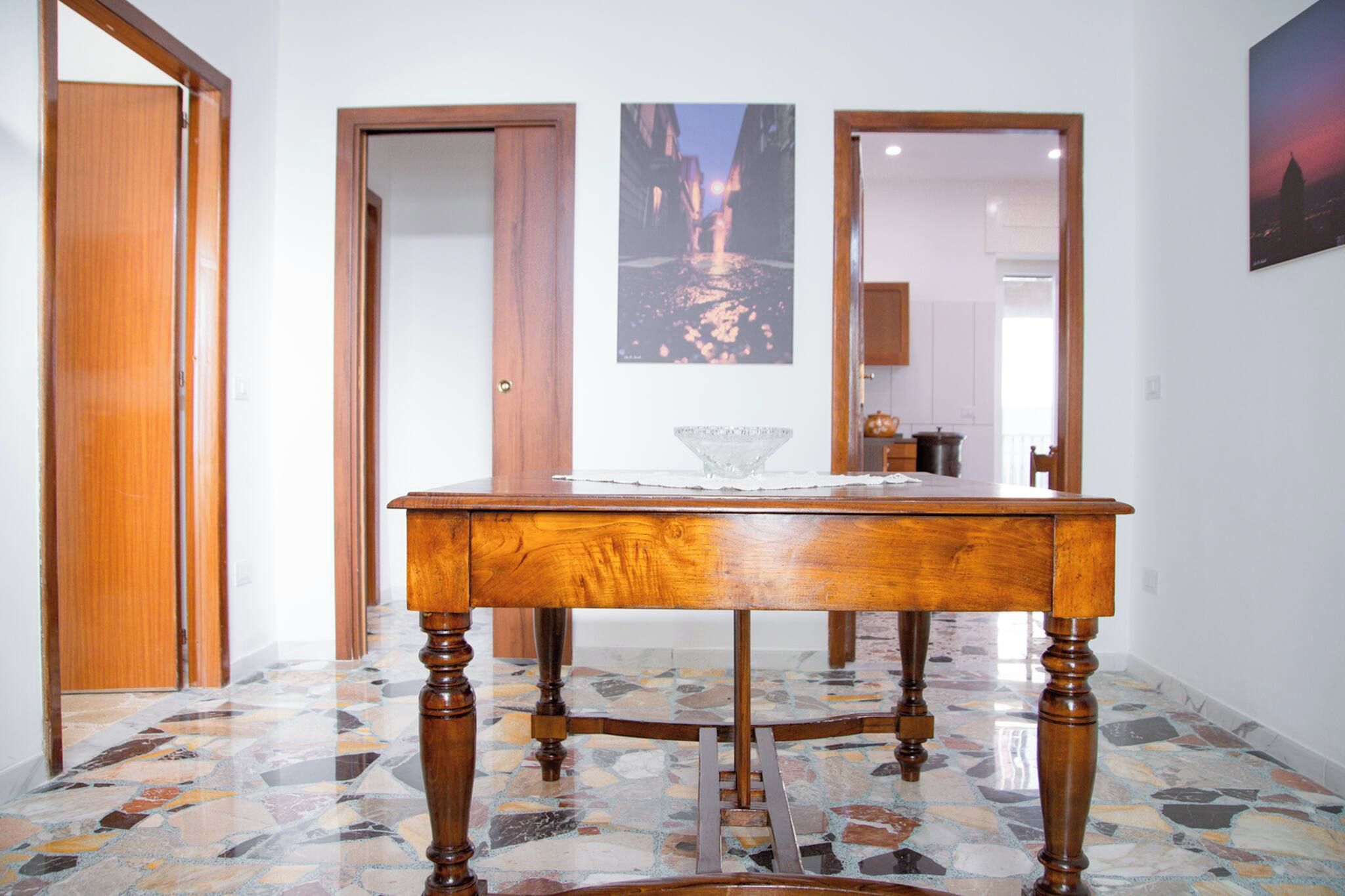 A dining table with a glass centerpiece in a room with tiled flooring and wooden doors.