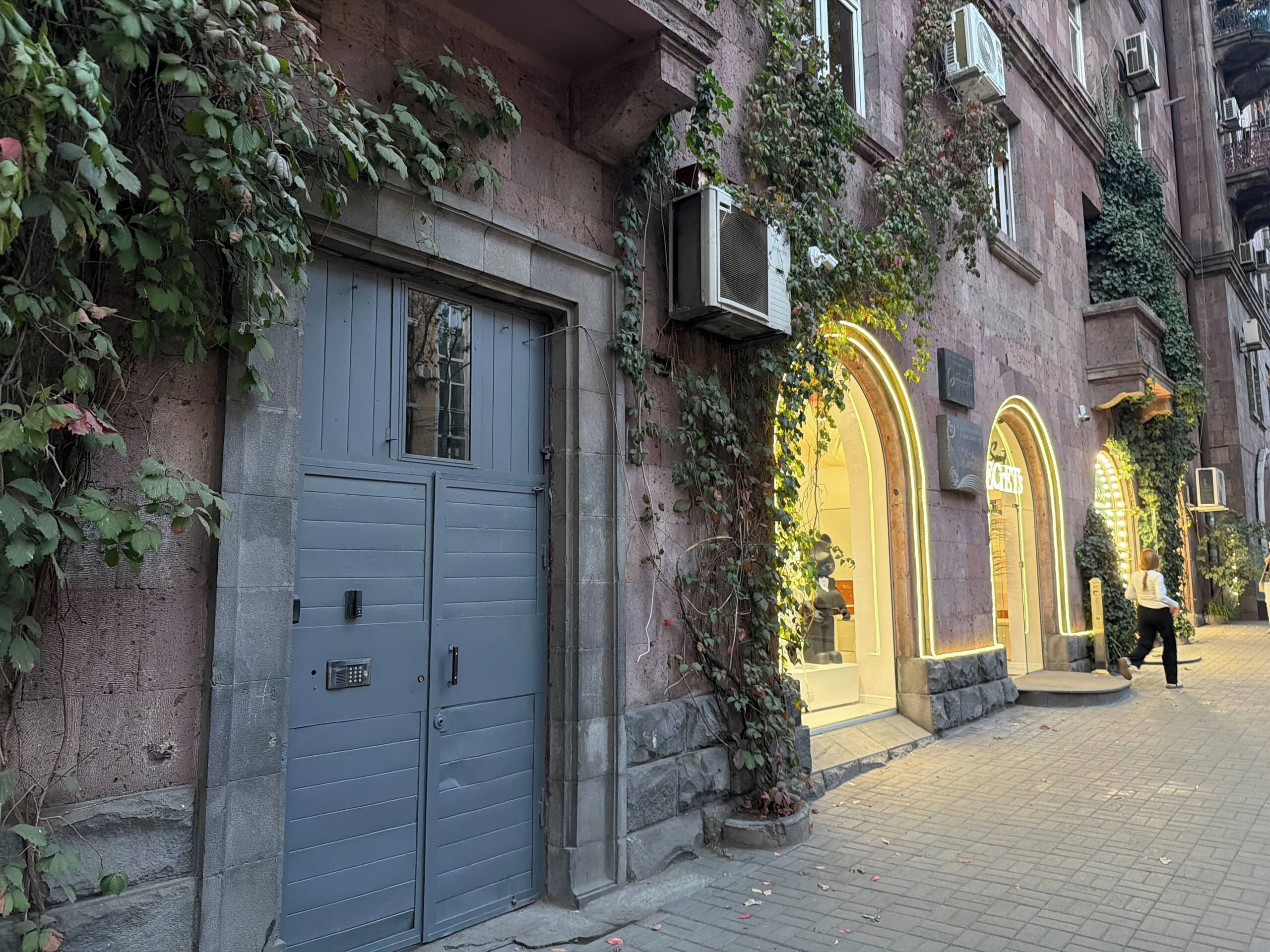 A building with a closed grey door, a window, and a shop with a yellow awning.
