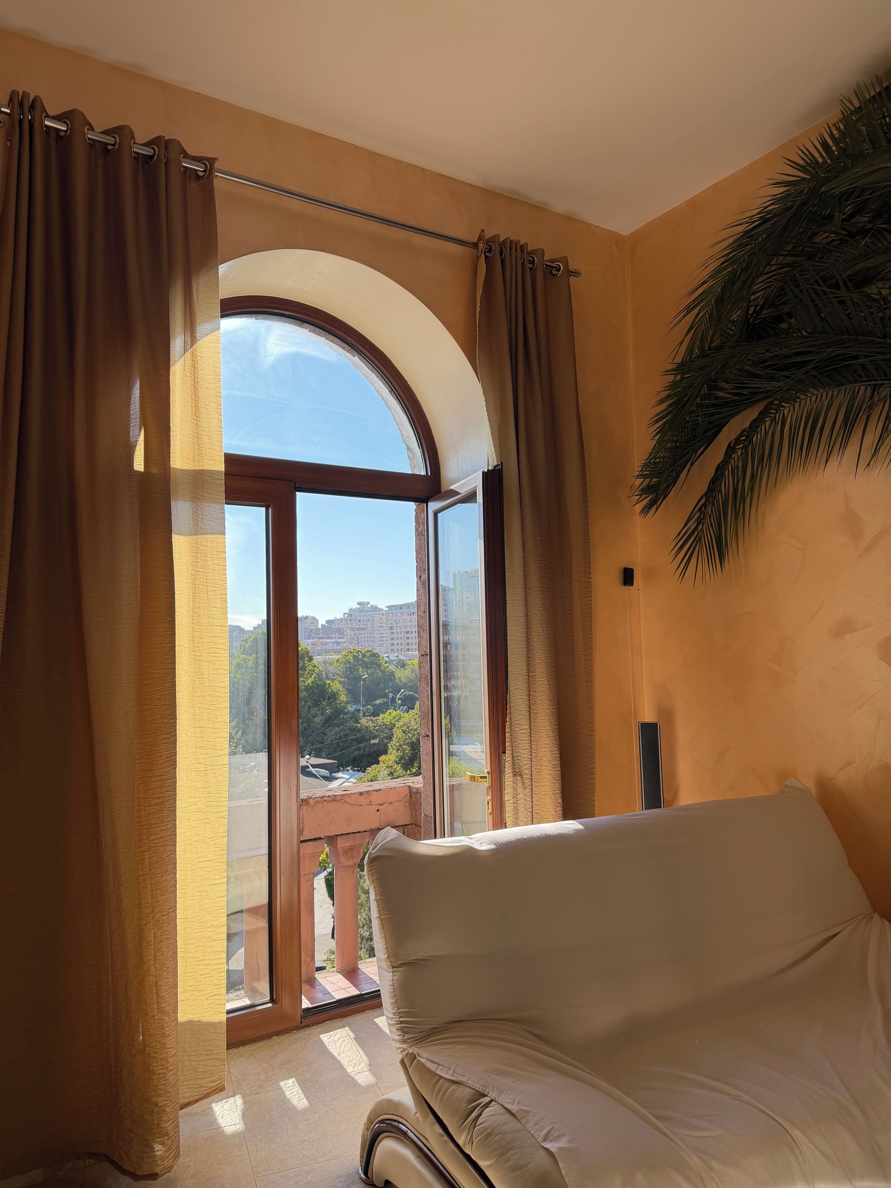 A room with a large window, a sofa, and a view of a cityscape.