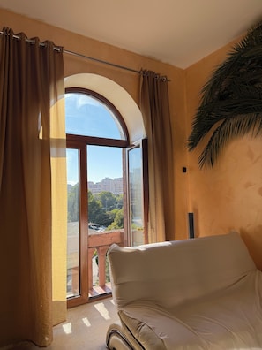 A room with a large window, a sofa, and a view of a cityscape.