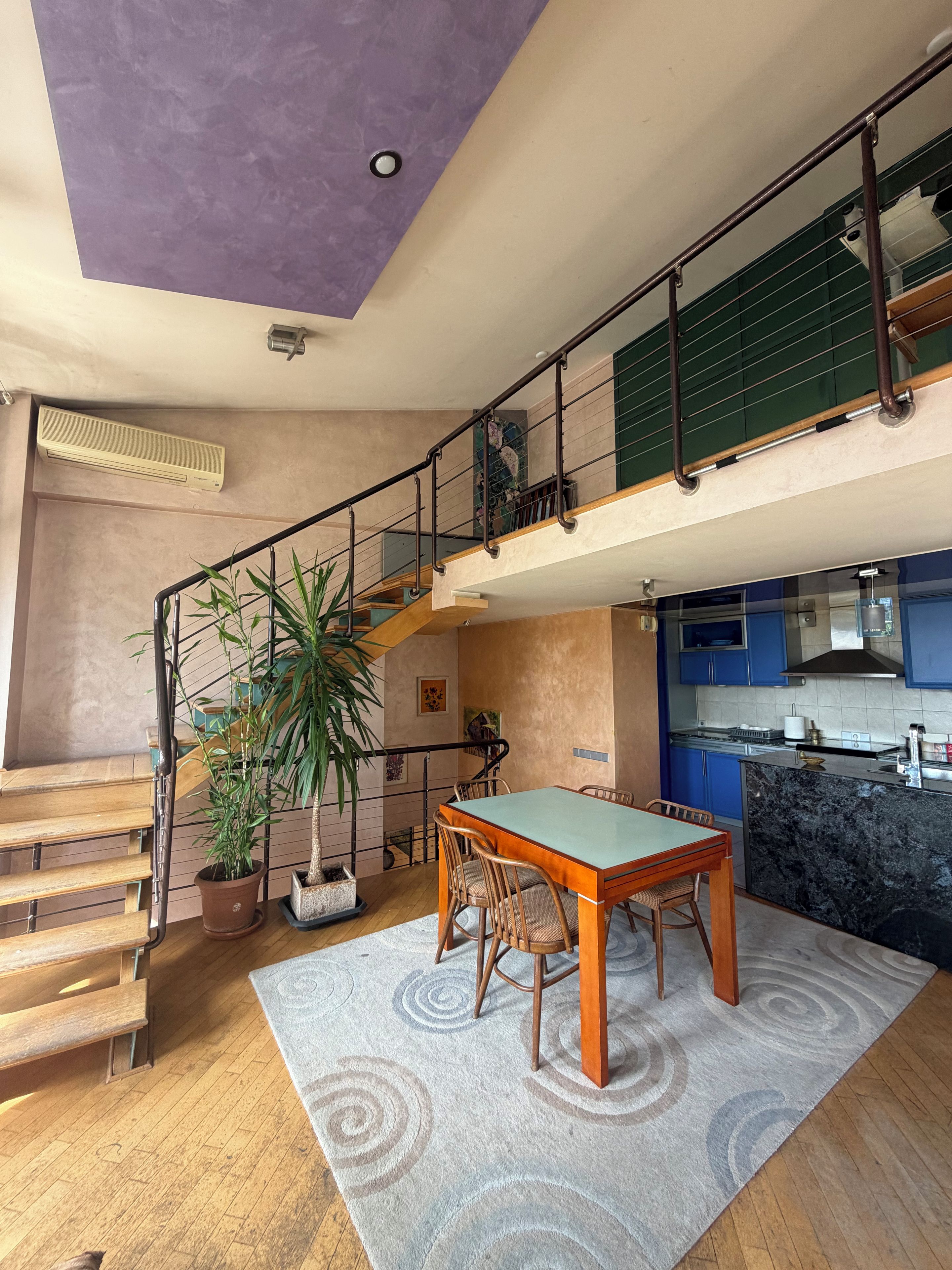 A spacious living area with a dining table, chairs, a staircase, and a kitchen area.