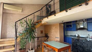 A spacious living area with a dining table, chairs, a staircase, and a kitchen area.
