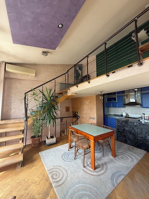 A spacious living area with a dining table, chairs, a staircase, and a kitchen area.