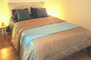 Una cama con edredón azul y marrón, una lámpara de noche y una mesita con lámpara.