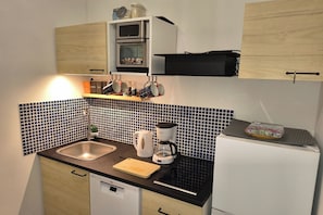 Una cocina compacta con microondas, cafetera, hervidor y un refrigerador pequeño.