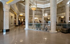 Un hall d’entrée spacieux, doté de hauts plafonds, de colonnes en marbre et de lustres décoratifs.