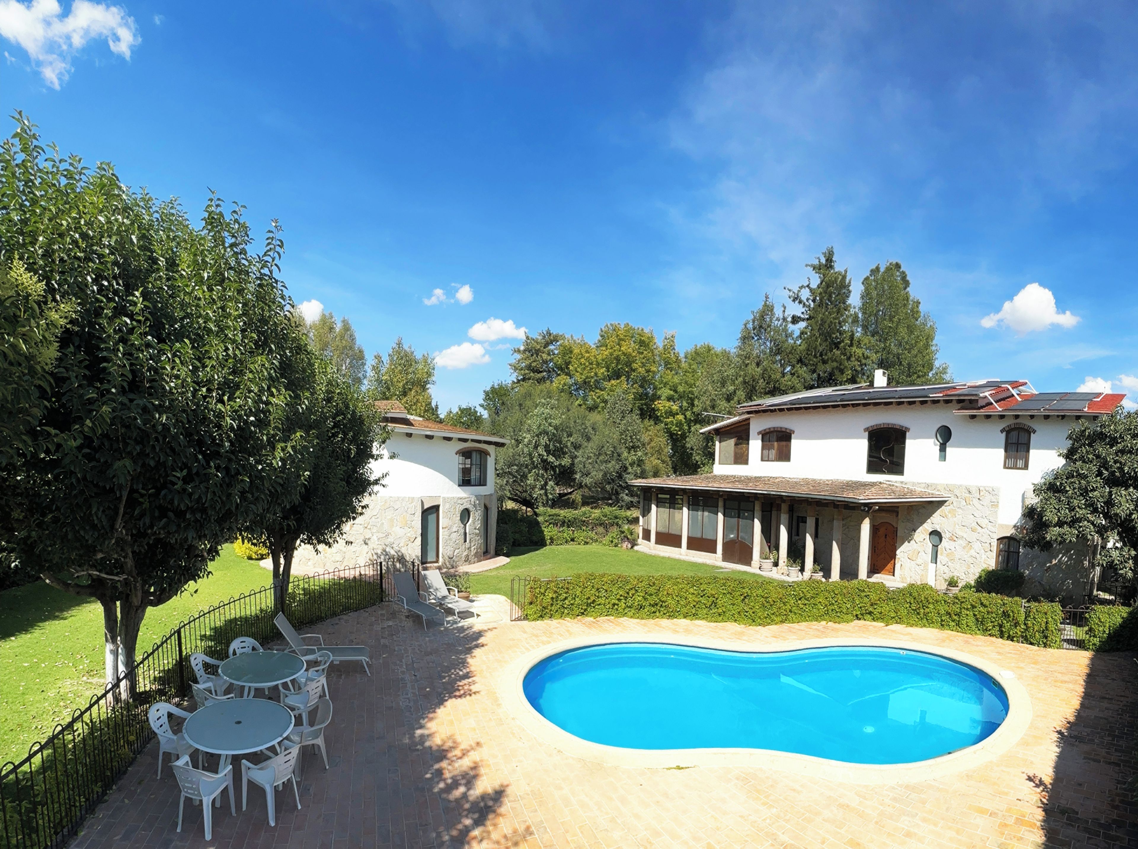 Ein zweistöckiges Haus mit Swimmingpool, umgeben von einem gepflegten Rasen und Bäumen.