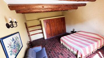 A bedroom with a brick floor, a wooden bed frame, a sofa, a wardrobe, and a wall-mounted light fixture.