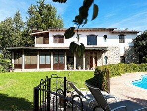 Une maison à deux étages avec une piscine, une pelouse bien entretenue et une terrasse dotée de chaises longues.
