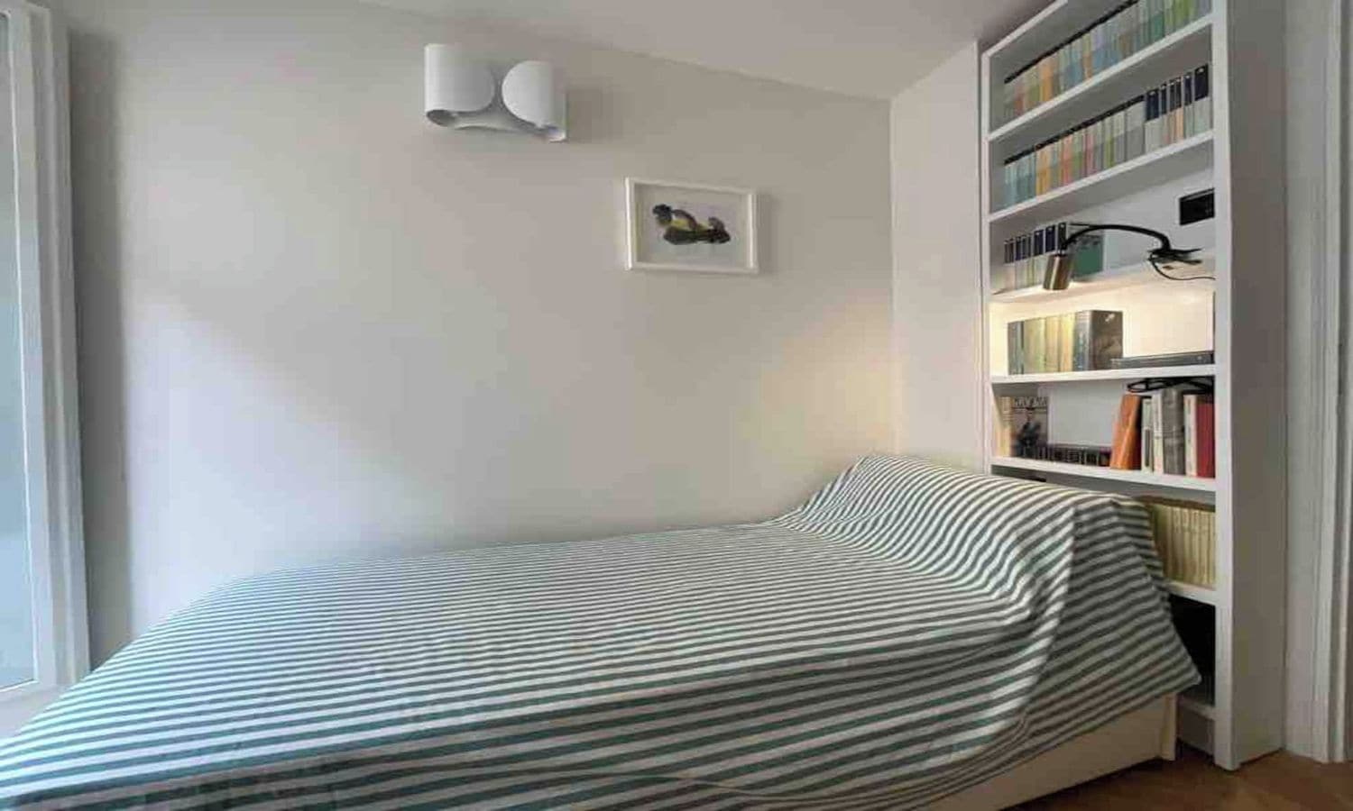 A small bedroom with a single bed, a bookshelf, and a framed picture on the wall.
