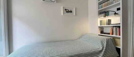 A small bedroom with a single bed, a bookshelf, and a framed picture on the wall.