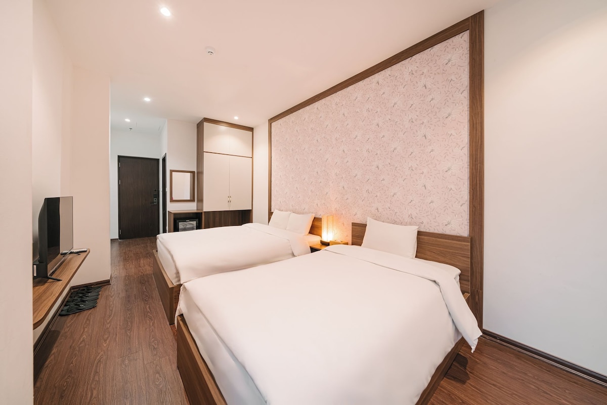 A hotel room with two beds, a television, a mirror, and a wooden floor.