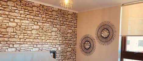 Een slaapkamer met een stenen muur, een bed met kussens, een hanglamp en uitzicht op buiten.