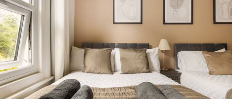 A hotel room with a bed, two pillows, a bedside table with a lamp, and two framed artworks on the wall.