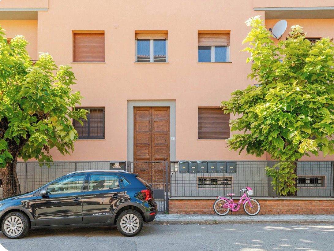Un edificio de fachada color beige, una puerta de madera y una bicicleta rosa estacionada afuera.