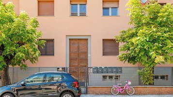 Un edificio de fachada color beige, una puerta de madera y una bicicleta rosa estacionada afuera.