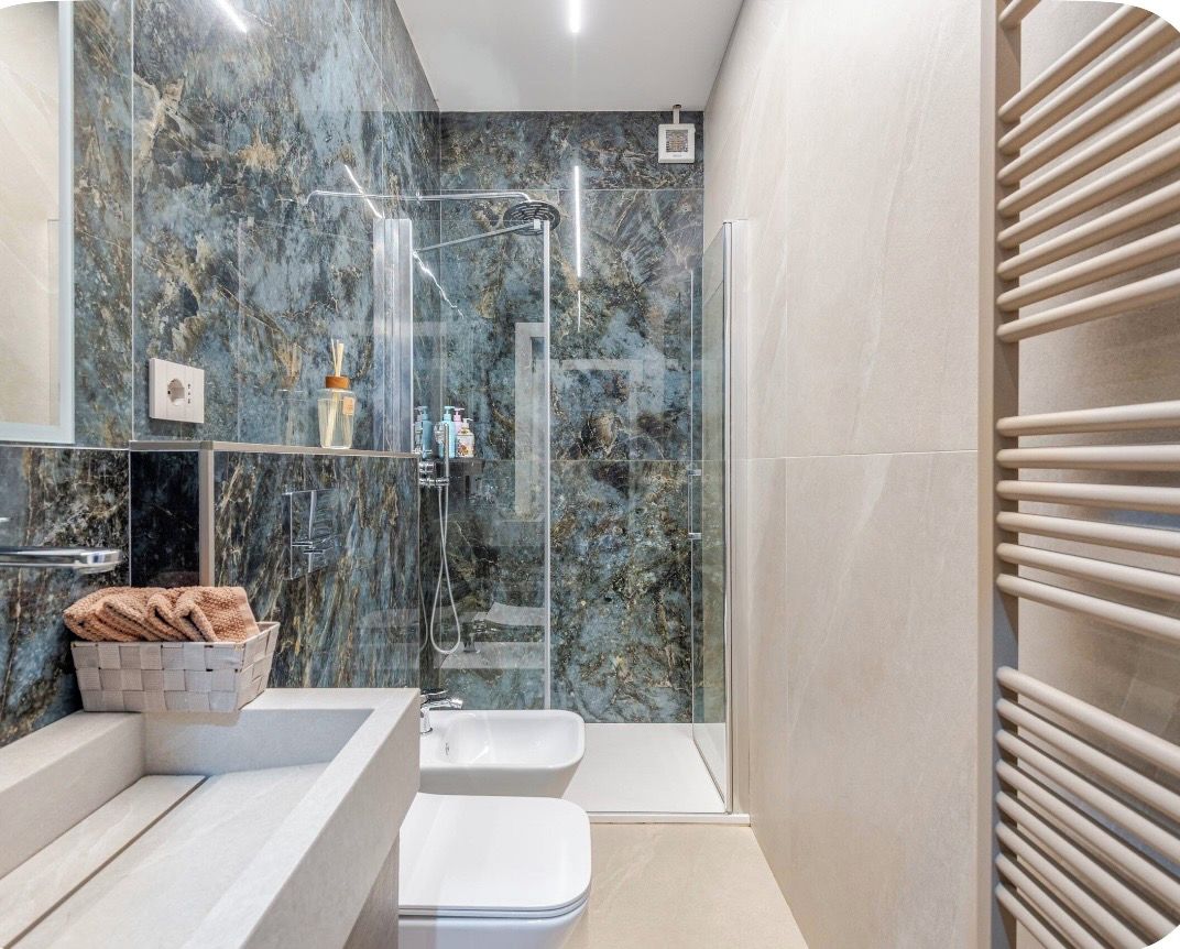A modern bathroom with a glass-enclosed shower, a white sink, and a marble wall.