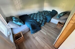 Een kleine kamer met een bed, twee kussens, een tafeltje en twee manden.