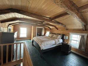 A wooden cabin bedroom with a bed, nightstands, and a desk. - Cozy artist's retreat with an incredible view (Keels)