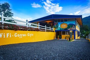 A building with a yellow exterior and a blue roof, featuring a mural of a person and a coffee cup. - Hotel Central Boquete  (Boquete)
