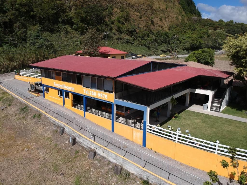 Un edificio amarillo con techo rojo, una cerca blanca y una carretera al frente.